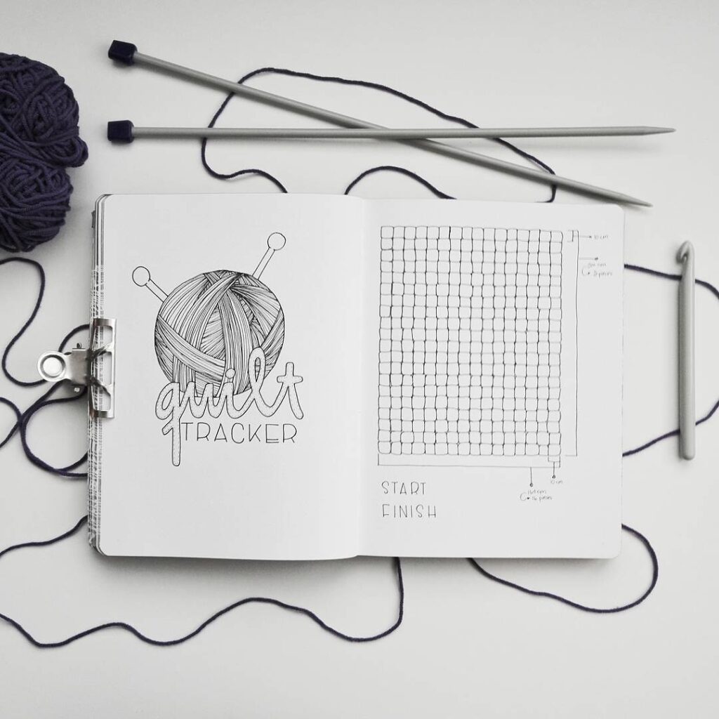 Knitting journal open to quilt tracker page with yarn and knitting needles nearby.