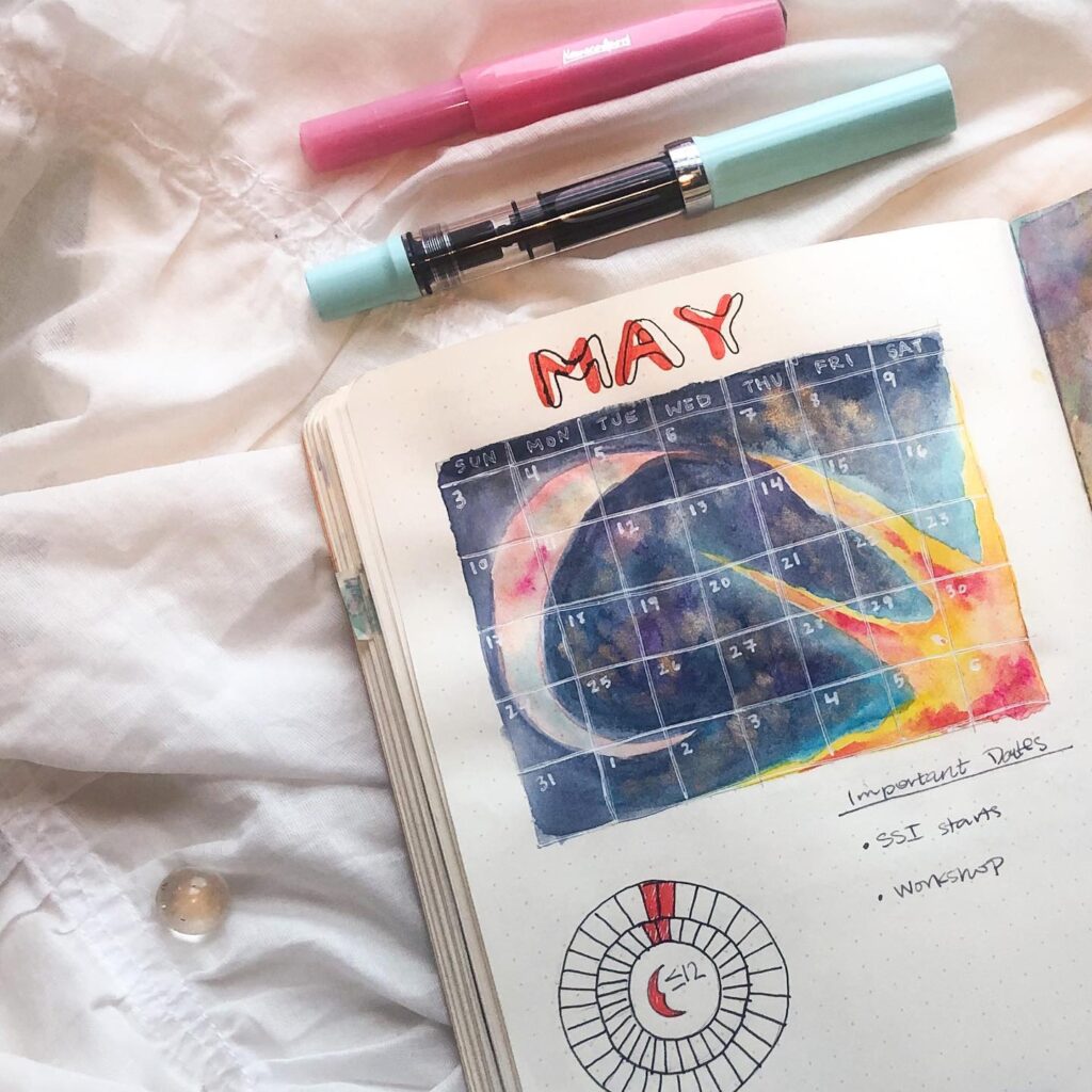 Handwritten bullet journal with colorful May calendar and markers on a white sheet, emphasizing planning.