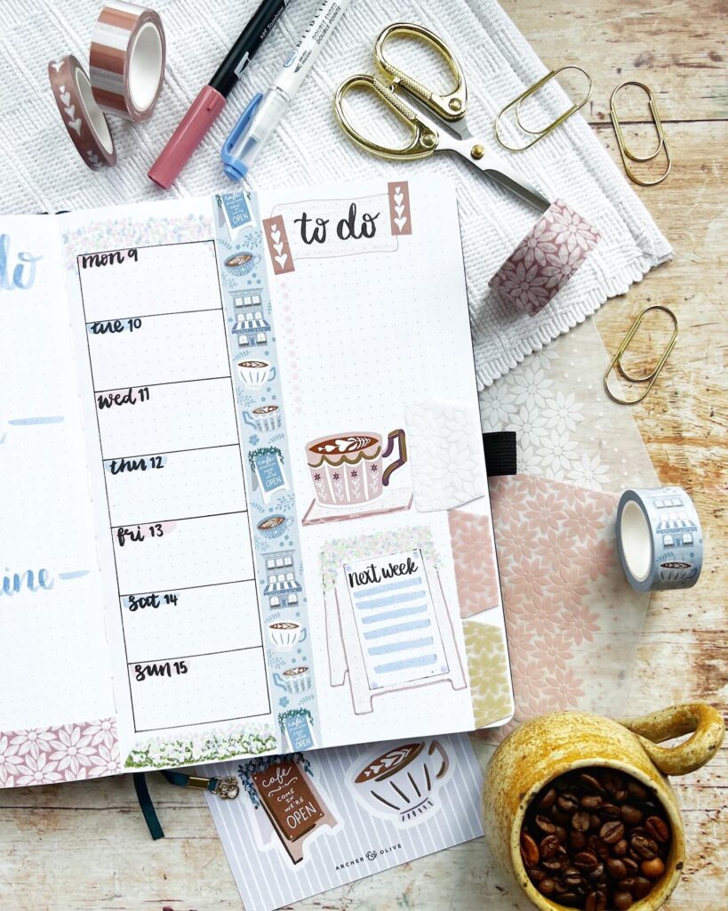 Bullet journal with to-do list, decorative tapes, pens, scissors, and coffee cup on a wooden table.