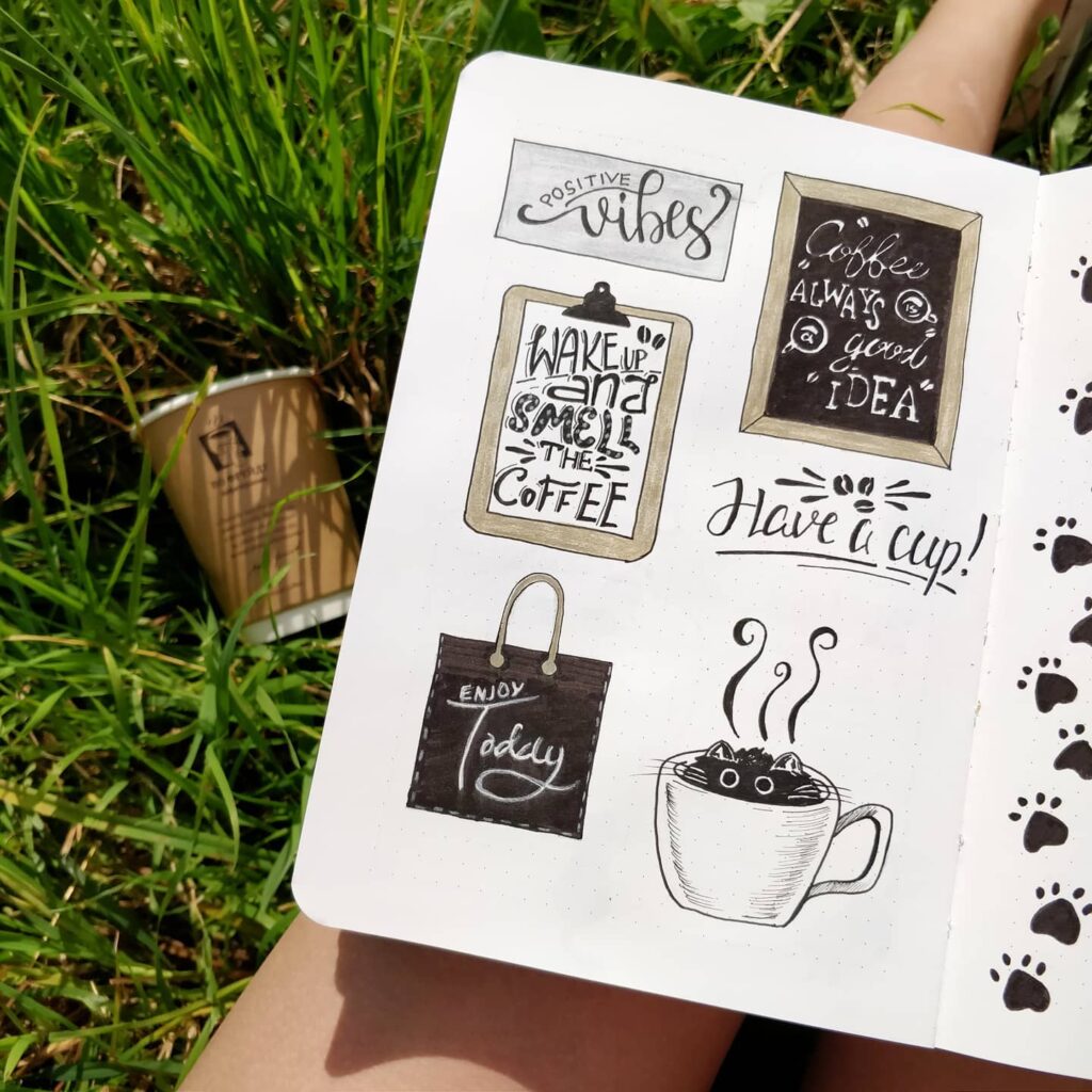 Hand-drawn coffee-themed doodles in a journal on grass, featuring uplifting quotes and a paper cup nearby.