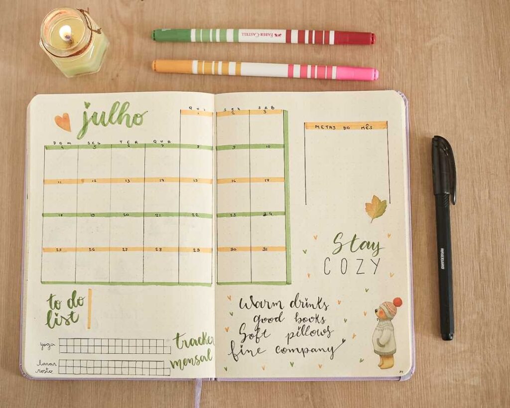 Bullet journal open to July with to-do list, monthly calendar, markers, and cozy decor on a wooden table.