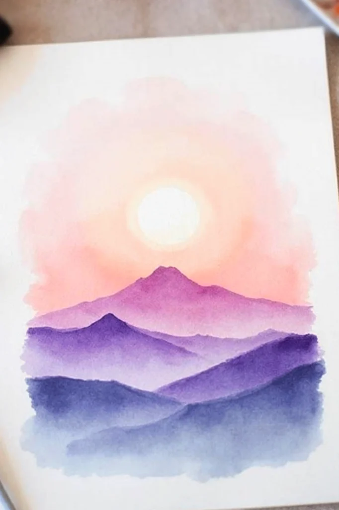 Watercolor landscape painting of a sunrise over purple mountains, with soft pink and orange sky.