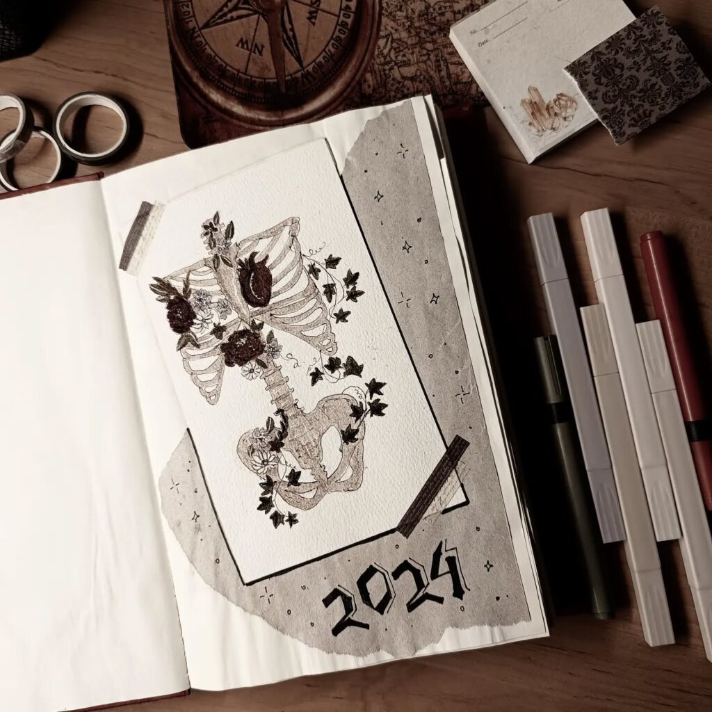 Open journal with skeleton art and plants for 2024, surrounded by markers and a compass for creative inspiration.