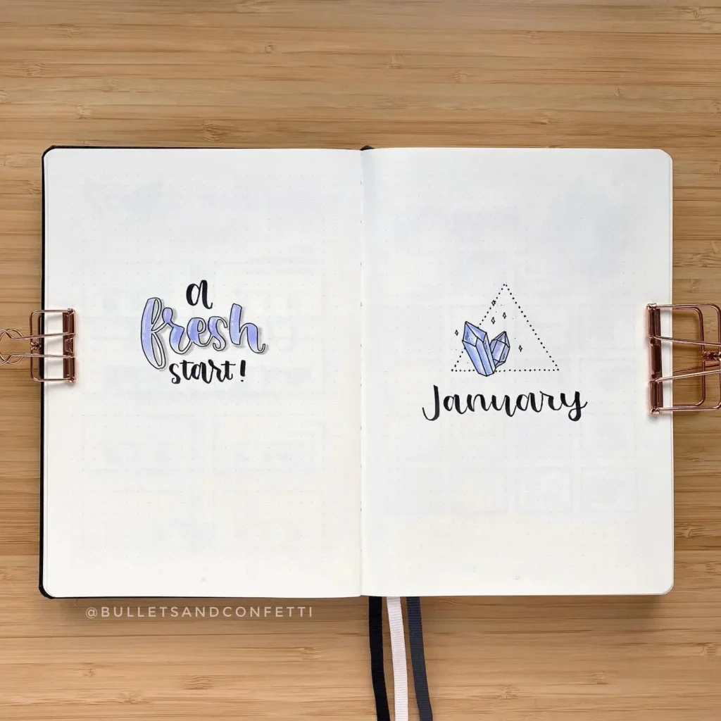 Bullet journal with “A fresh start!” and “January” written artistically on open pages, featuring crystal and triangle designs.