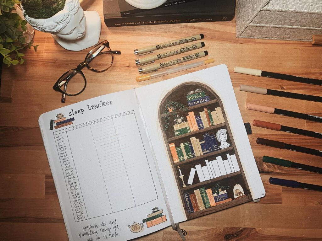 Bullet journal open to sleep and mood tracker pages, surrounded by pens, glasses, and books on a wooden desk.