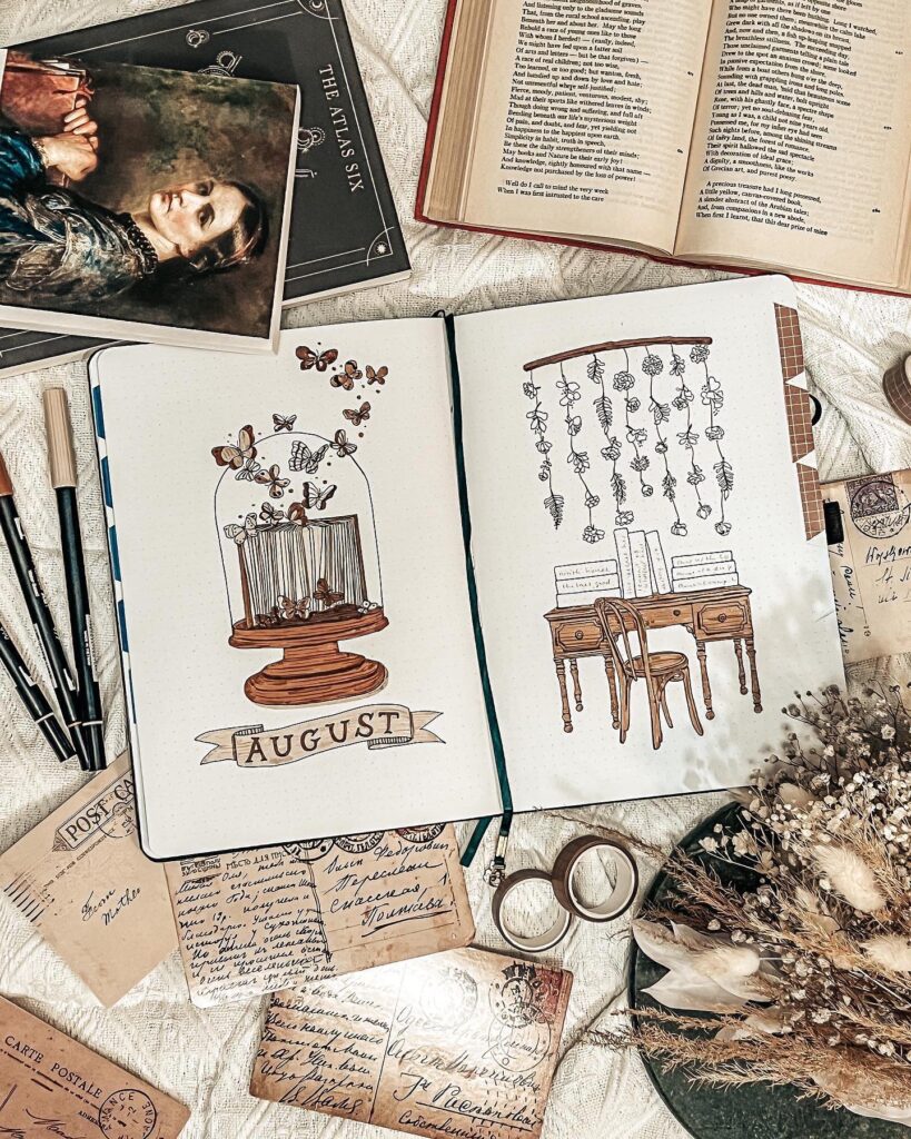 Open book with August journal illustrations, surrounded by vintage postcards, dried flowers, and stationery.