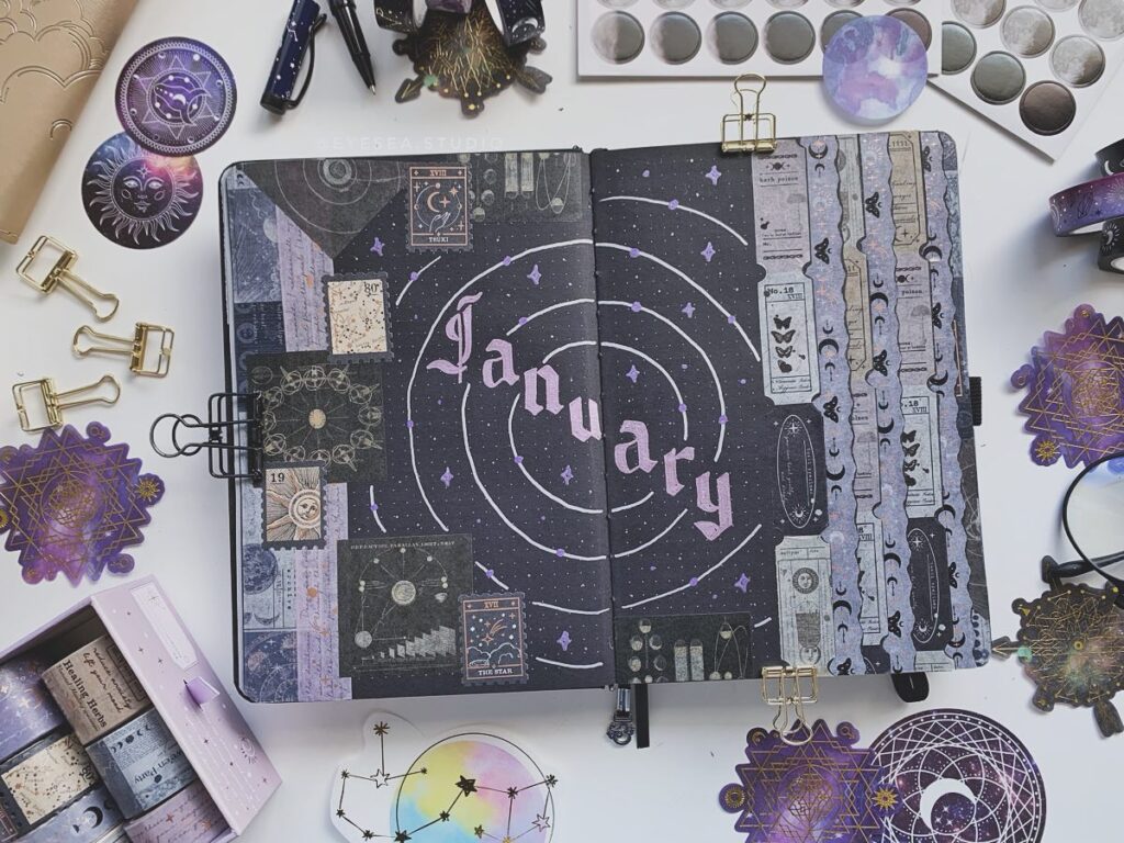 Bullet journal for January with celestial and mystical designs, surrounded by decorative stationery items.