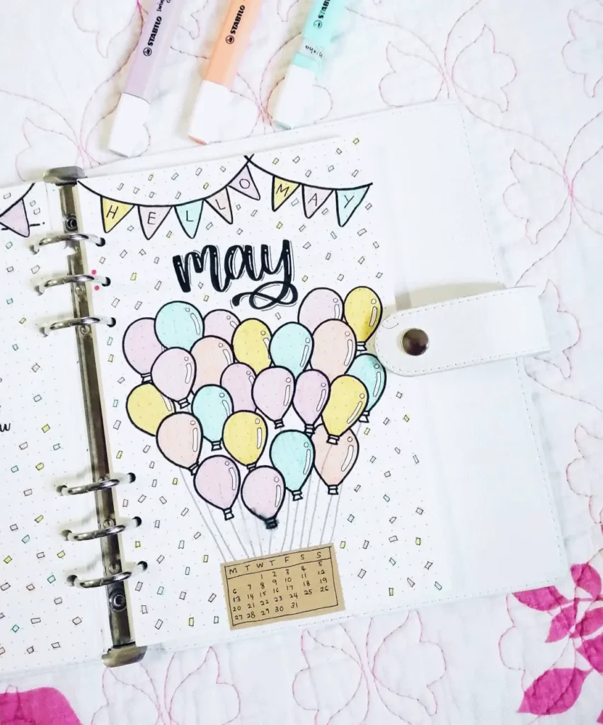 Colorful Hello May planner page with pastel balloons and a mini calendar, surrounded by markers on a floral background.