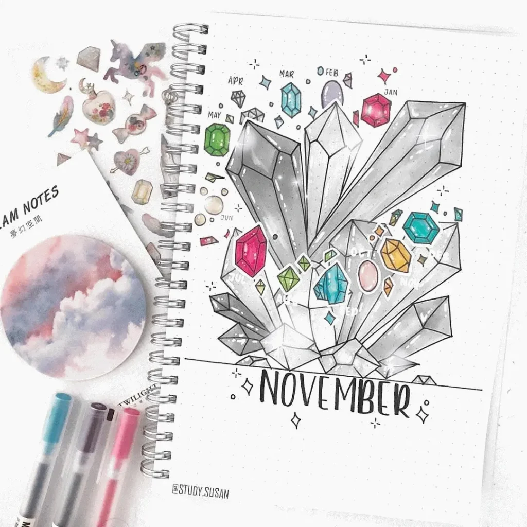 Bullet journal page with crystal designs for November, surrounded by colorful art supplies and stickers.
