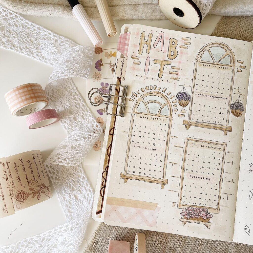 Bullet journal habit tracker with vintage decor, lace ribbons, and washi tape for planning and organization.
