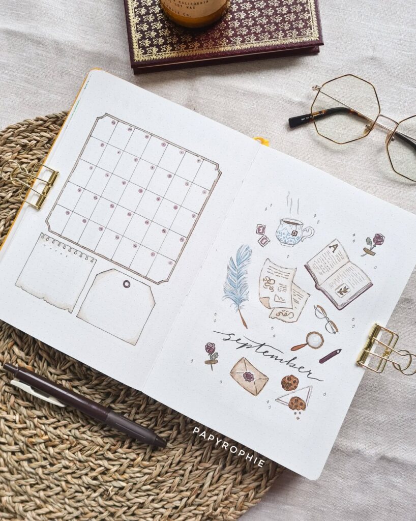 Open bullet journal with hand-drawn September calendar and cozy illustrations, surrounded by glasses and a pen.