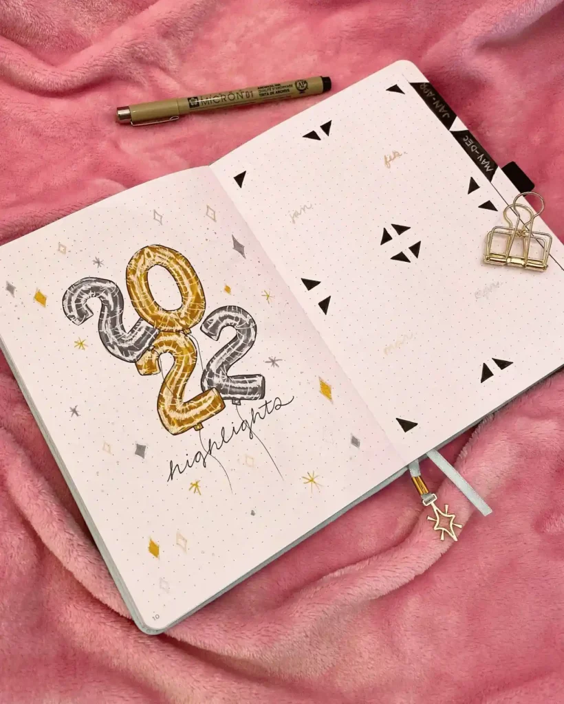 Open bullet journal on pink fabric, featuring 2022 highlights with artistic lettering and embellishments.