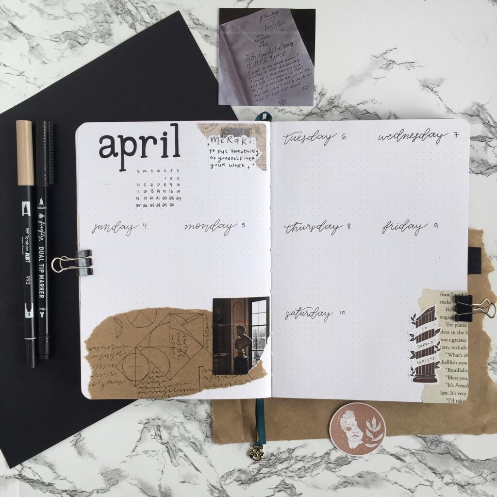 Open journal planner for April with artistic designs, surrounded by pens on a marble surface.