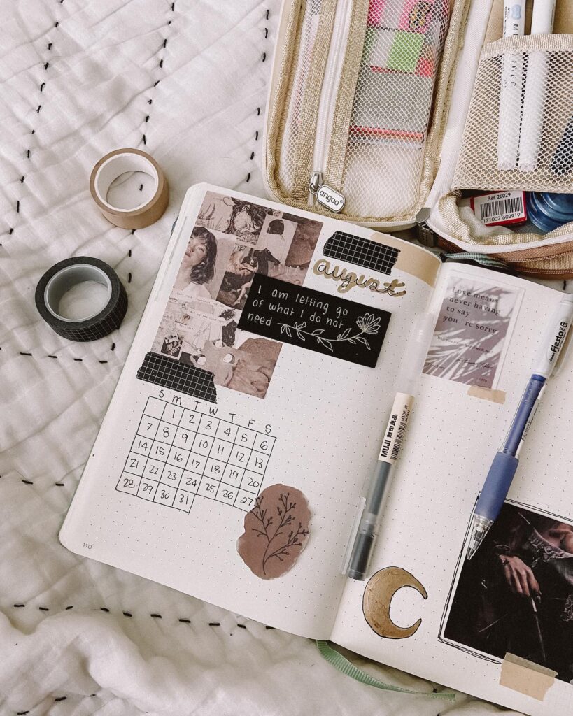 Bullet journal with August calendar, art, and quotes. Pens and washi tapes on a bed create a cozy creative setup.