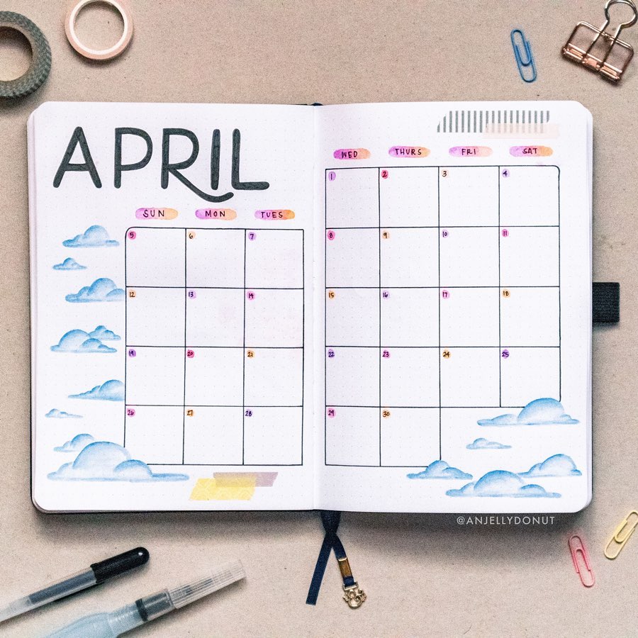 April bullet journal layout with hand-drawn clouds, colorful days, and office supplies nearby.