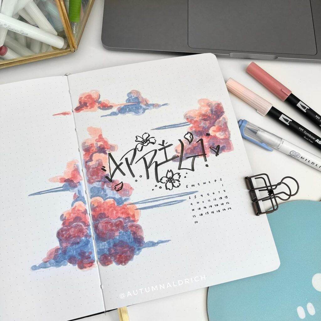 April bullet journal spread with colorful clouds, calendar, and stationery on desk.