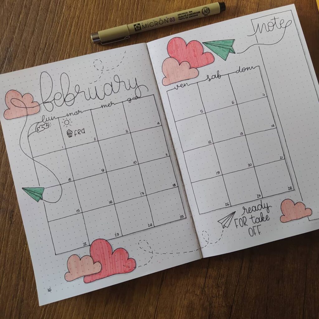 Hand-drawn February bullet journal calendar with hearts and paper plane theme on a wooden table.