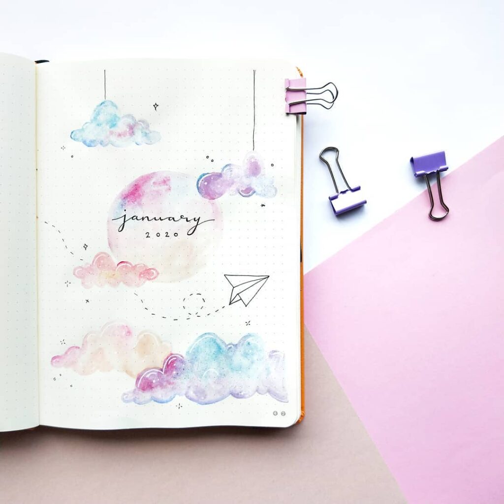Bullet journal page for January 2020 with pastel clouds and paper airplane, arranged with purple binder clips.