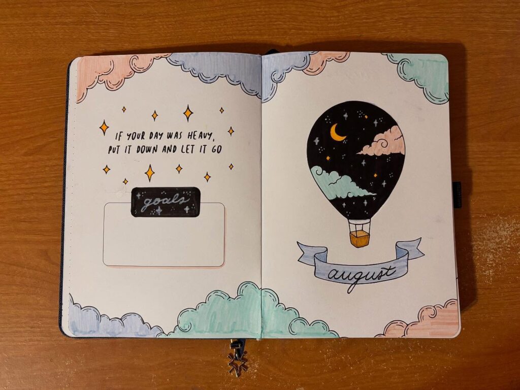 Bullet journal with a motivational quote and hot air balloon drawing for August on a wooden table.