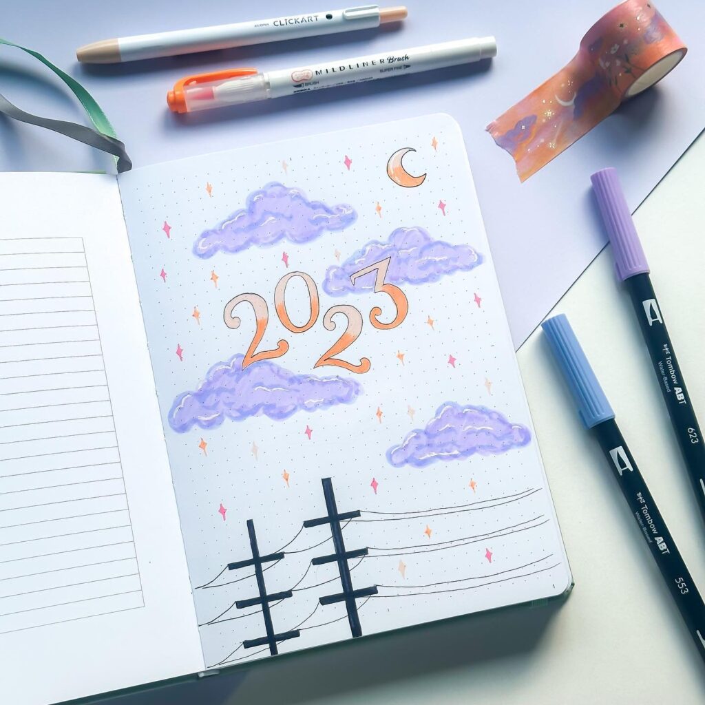 Bullet journal spread for 2023 with pastel clouds, pens, and celestial-themed washi tape.