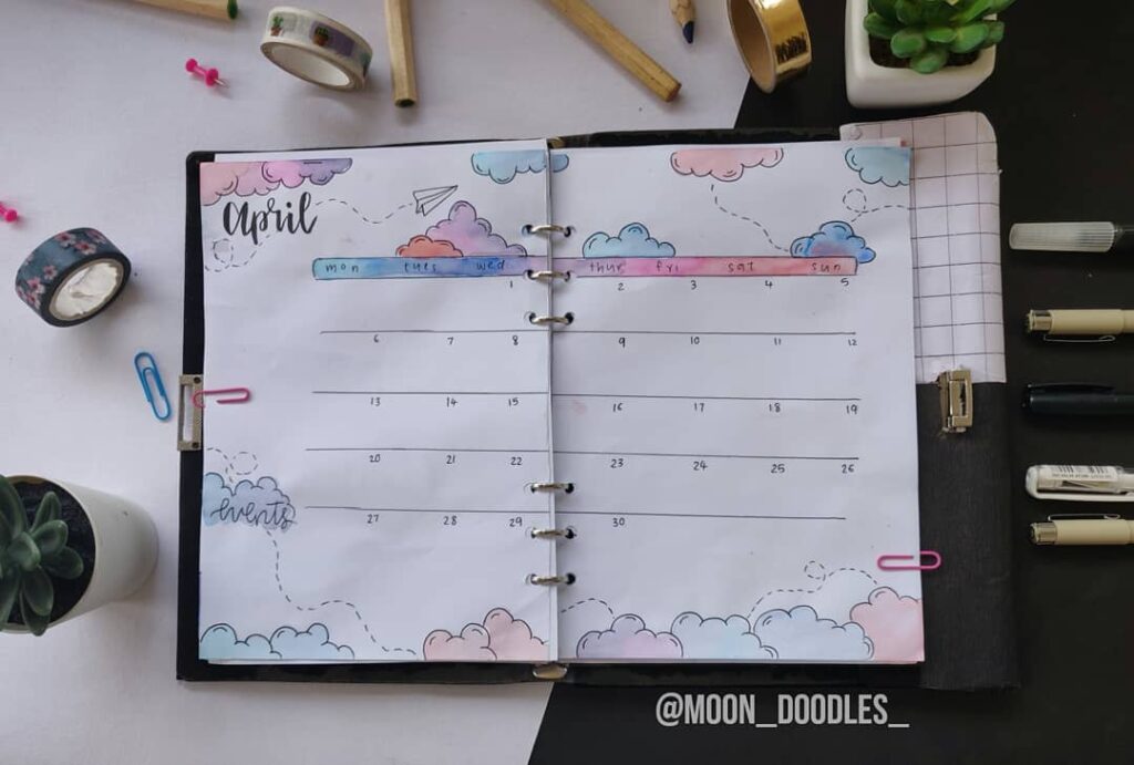 Colorful April bullet journal layout with cloud doodles and stationery items.
