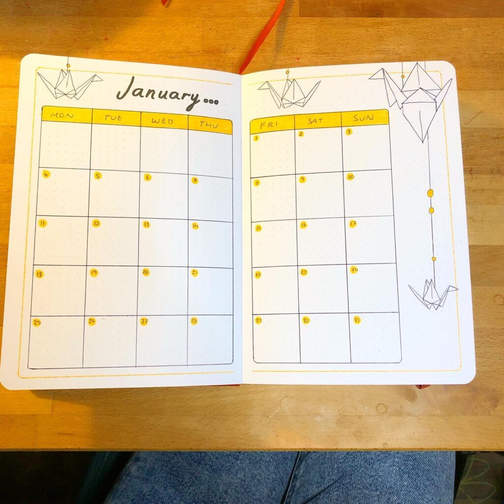 January bullet journal calendar with origami crane design on a wooden table.