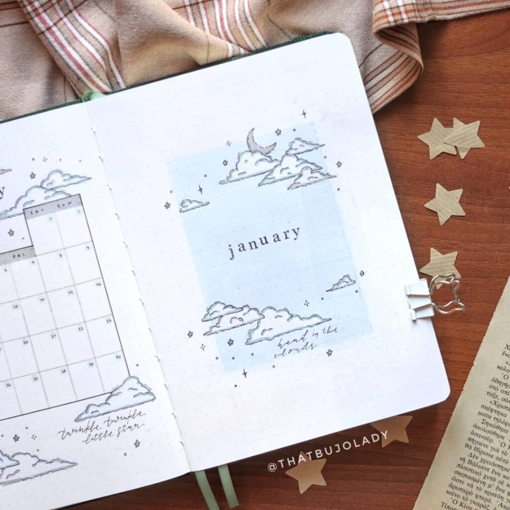 January bullet journal spread with cloud doodles and calendar, cozy setup with fabric and star cutouts.