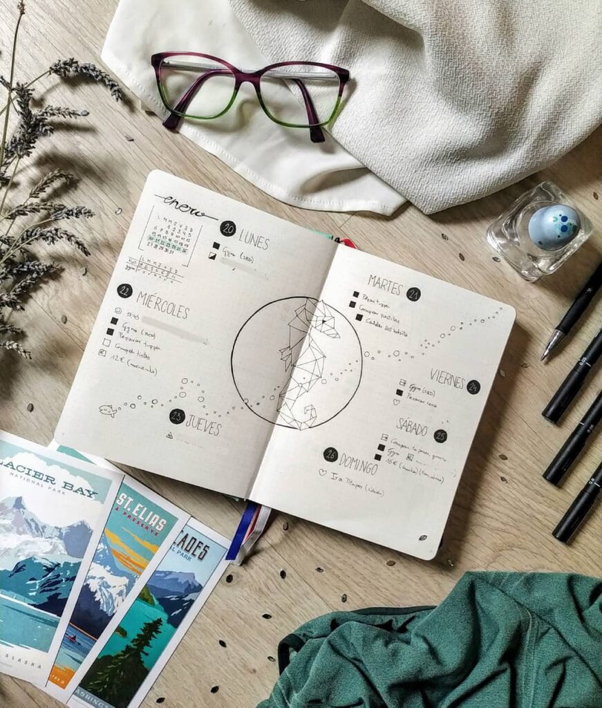 Open planner with handwritten schedule, glasses, pens, and travel brochures on a wooden desk. Cozy and organized workspace.