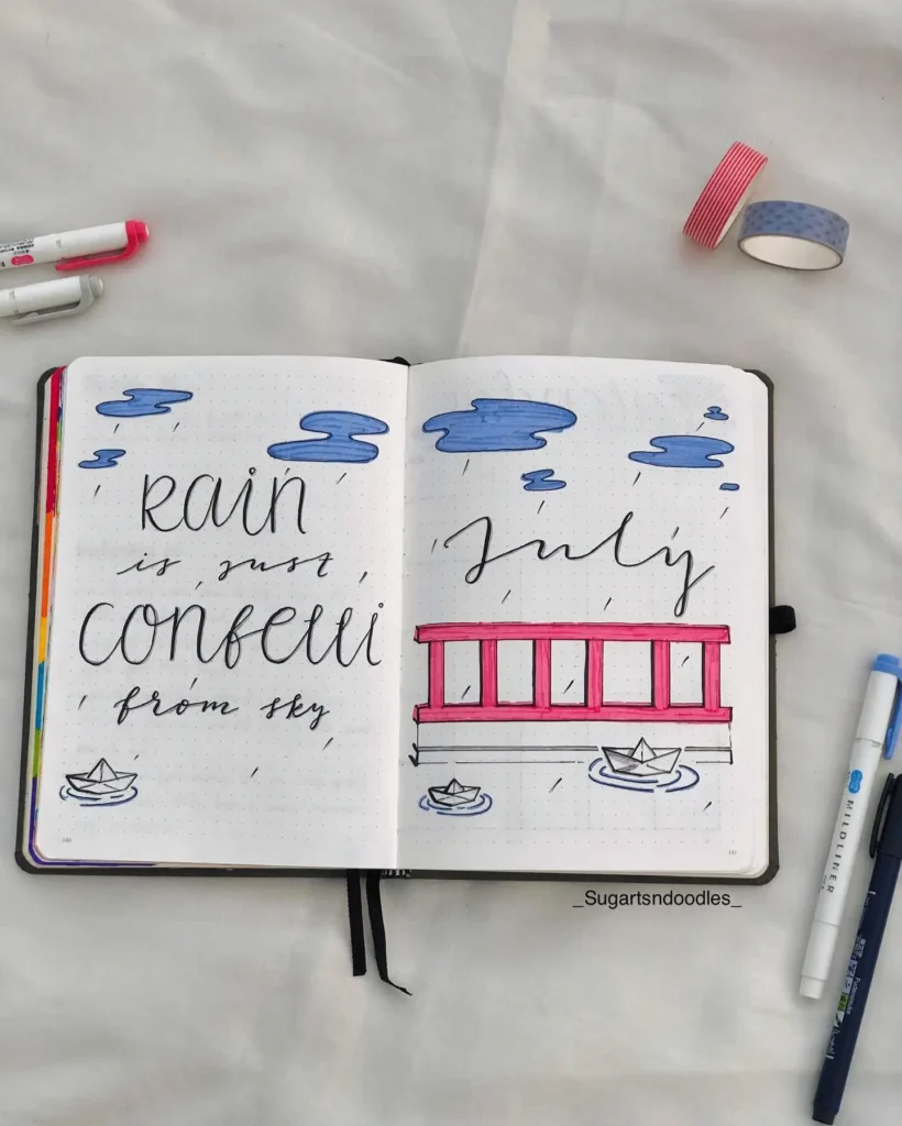 Open journal with artistic July theme, featuring clouds, rain, paper boats, and a pink bridge on dotted pages.