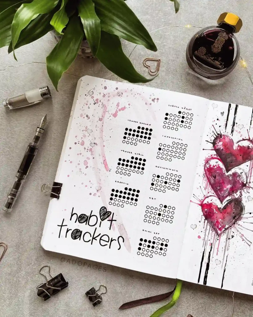 Bullet journal habit tracker with artistic heart design, surrounded by plant, ink, and pen on a gray desk.
