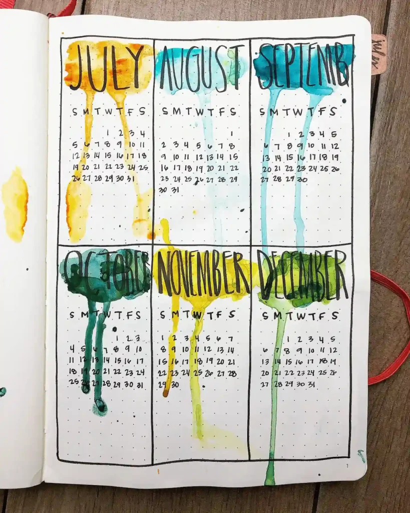 Watercolor-themed bullet journal calendar for July to December on a wooden table.