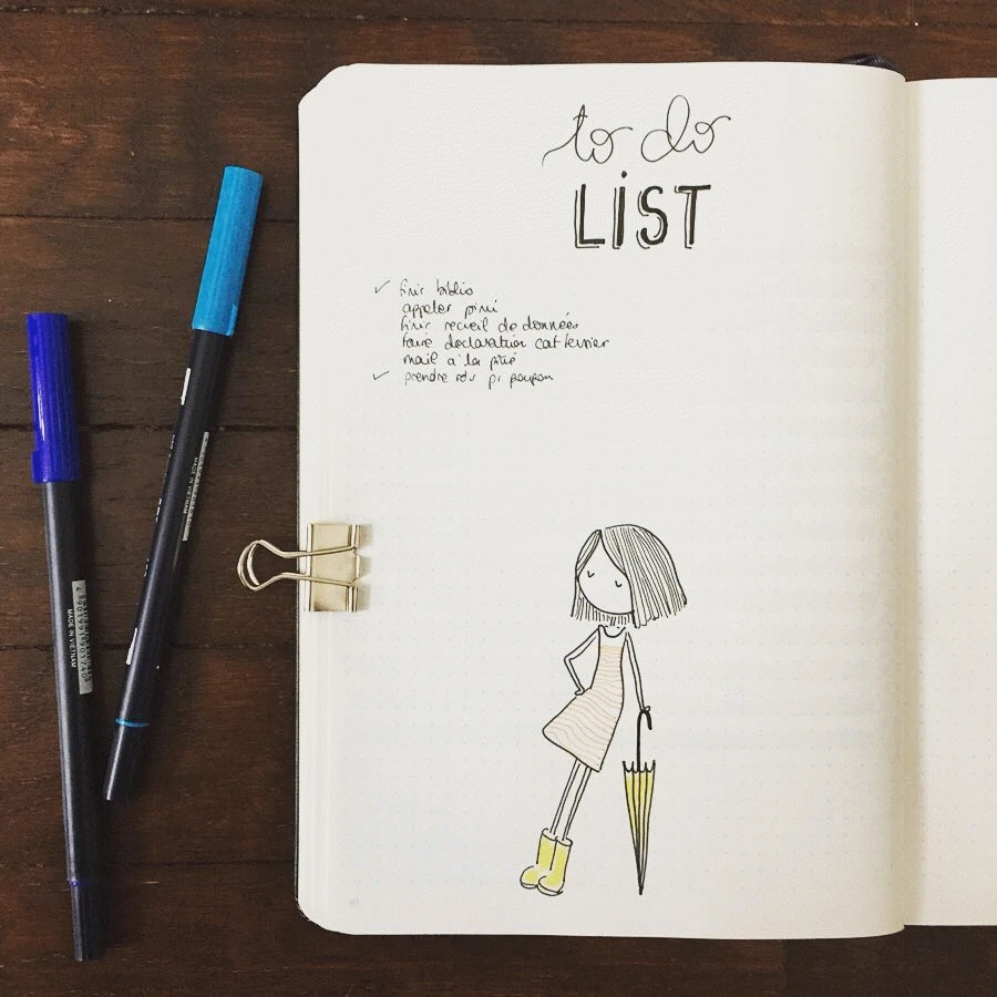 Open notebook with a handwritten to-do list, colorful pens, and a whimsical drawing of a girl with an umbrella.