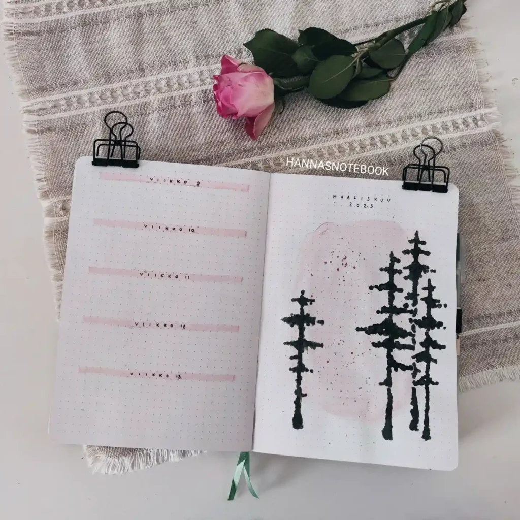 Open notebook with pink rose on cloth, featuring tree sketches and planner layout for March 2023.
