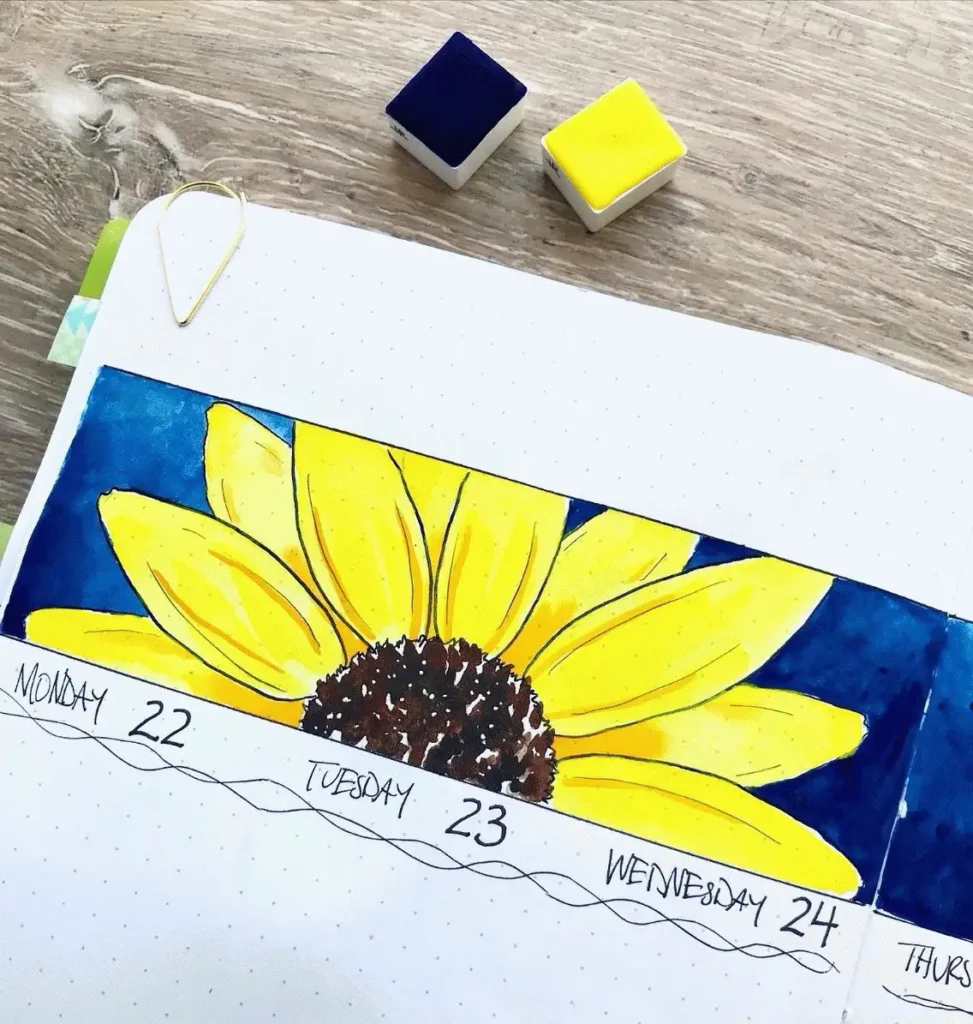 Hand-drawn sunflower in planner spread for Monday to Wednesday, with ink pads on a wooden table background.