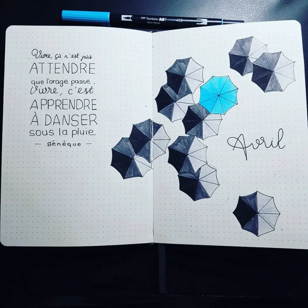 Open notebook with French quote, black and blue umbrellas, and the word Avril written on the page.