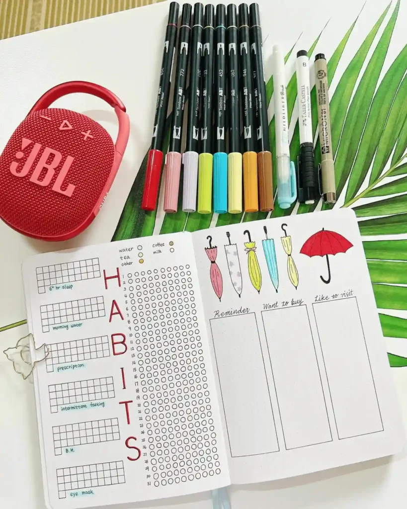 Bullet journal with habit tracker, colorful pens, and a red JBL speaker on a green leaf background.