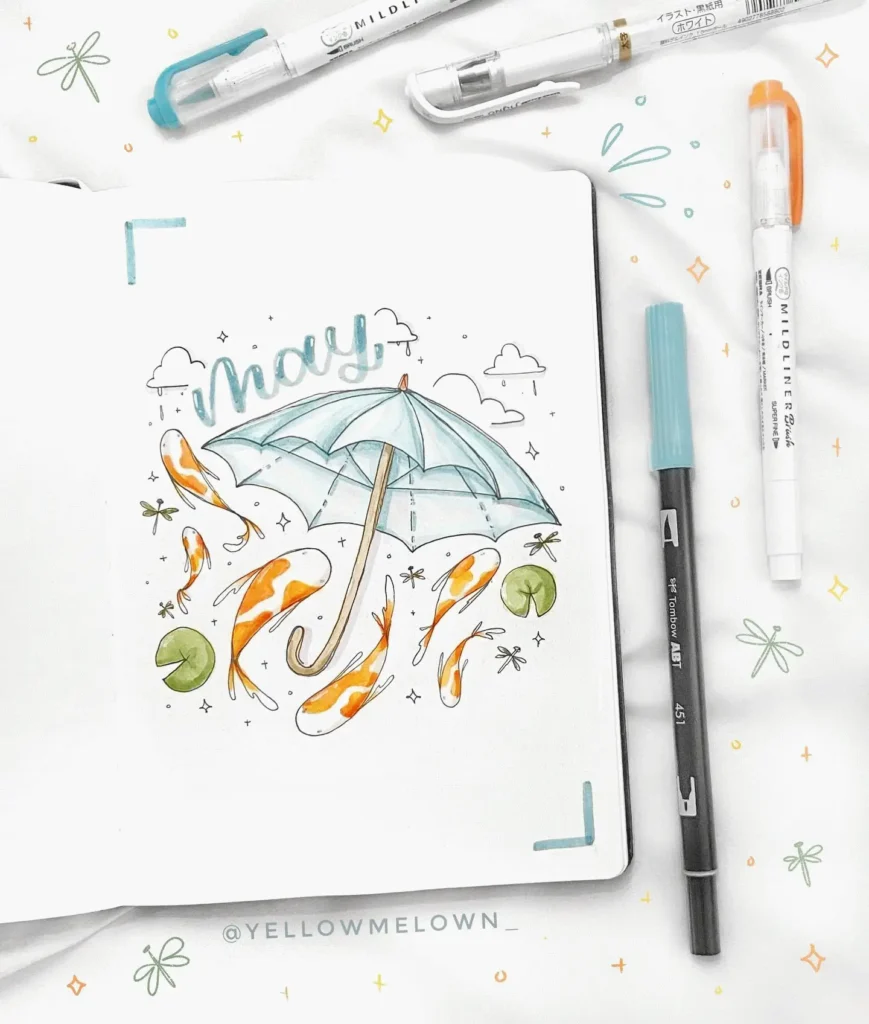Bullet journal page for May featuring koi fish and umbrella illustration, surrounded by pens and markers.