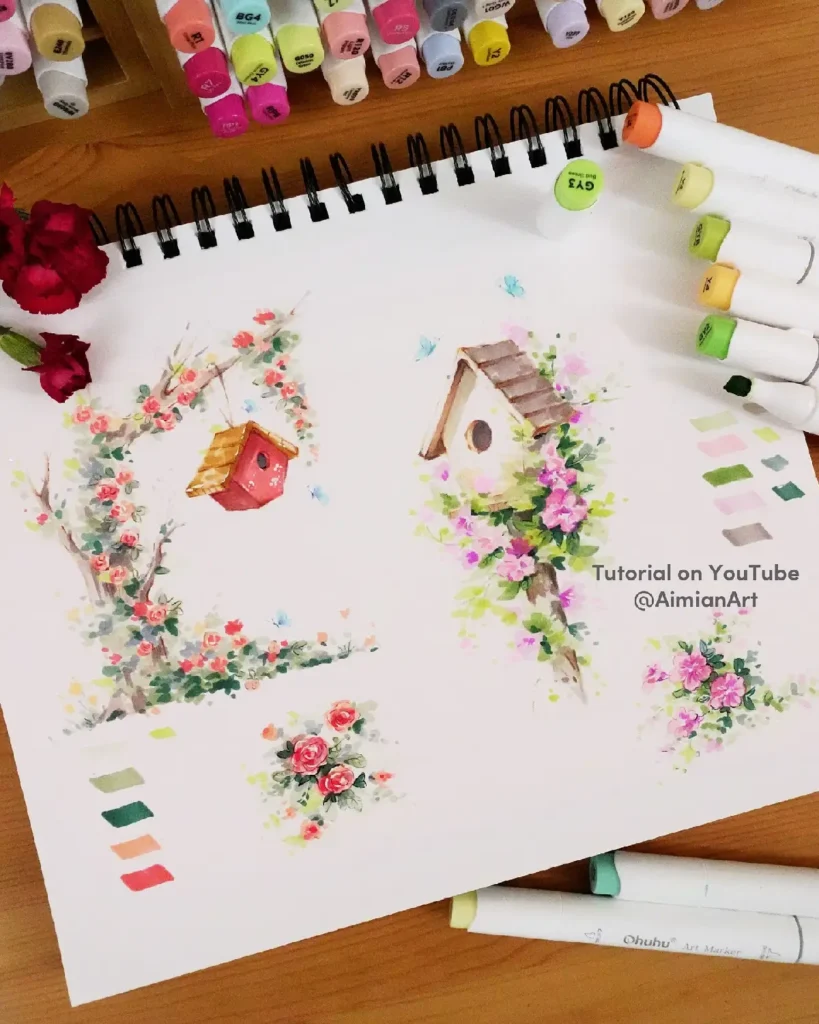 Colorful hand-painted flowers and birdhouses on a sketchbook, surrounded by art markers. Tutorial available on YouTube.