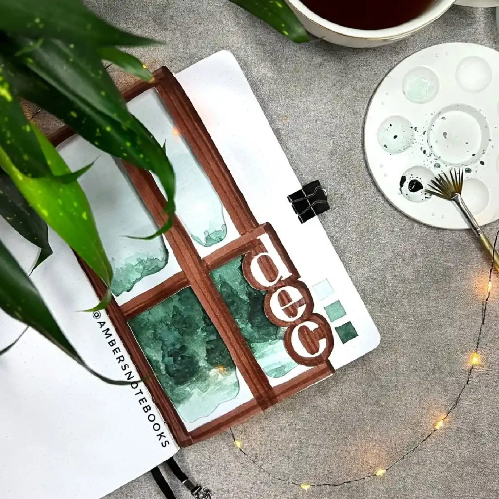 A creative bullet journal spread featuring a watercolor window illustration for December, surrounded by plants and art supplies.