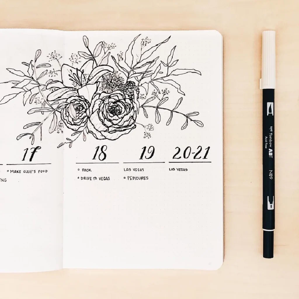 Bullet journal page with floral design, including plans for Las Vegas and daily tasks, beside a black pen.