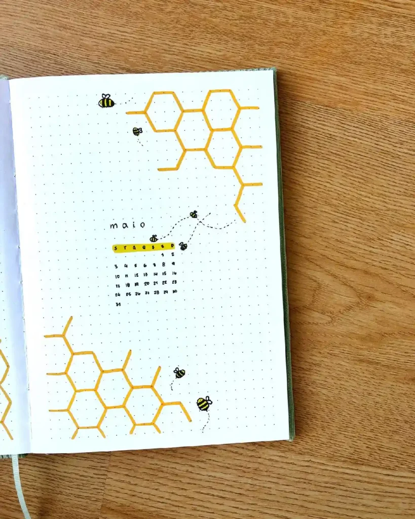 Bullet journal page for May featuring bees, honeycomb design, and a monthly calendar in a dotted notebook.
