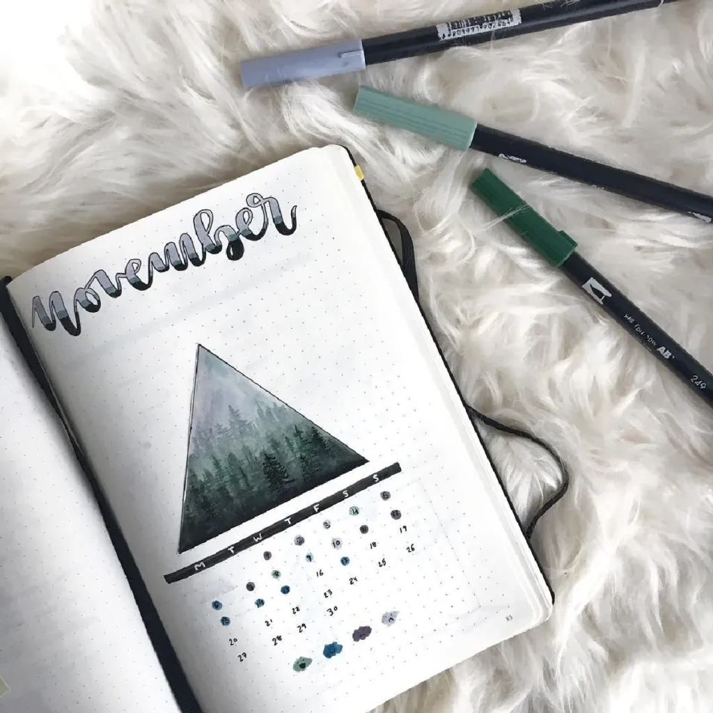 November bullet journal spread with a triangular forest illustration and colorful markers on a soft background.