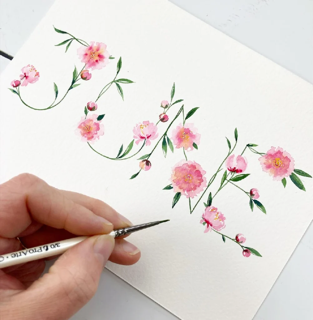 Hand painting pink florals with a fine brush on textured paper, showcasing beautiful watercolor techniques and artistry.