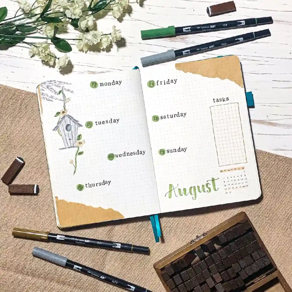 Aesthetic bullet journal layout for August, featuring days of the week and decorative elements, along with markers and flowers.