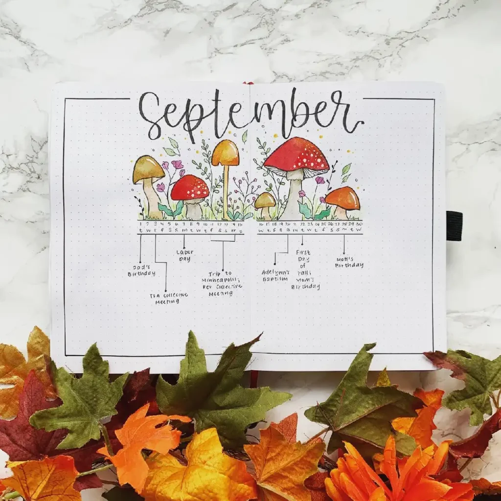 Colorful September bullet journal layout with mushrooms, flowers, and autumn leaves on a marble surface.