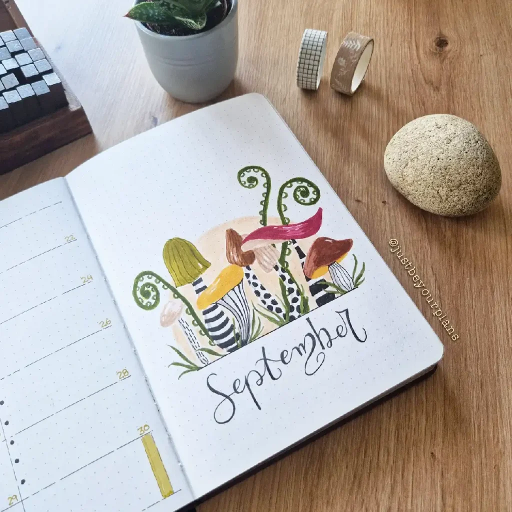 Hand-painted September illustration in a bullet journal, featuring colorful mushrooms and a cozy workspace aesthetic.