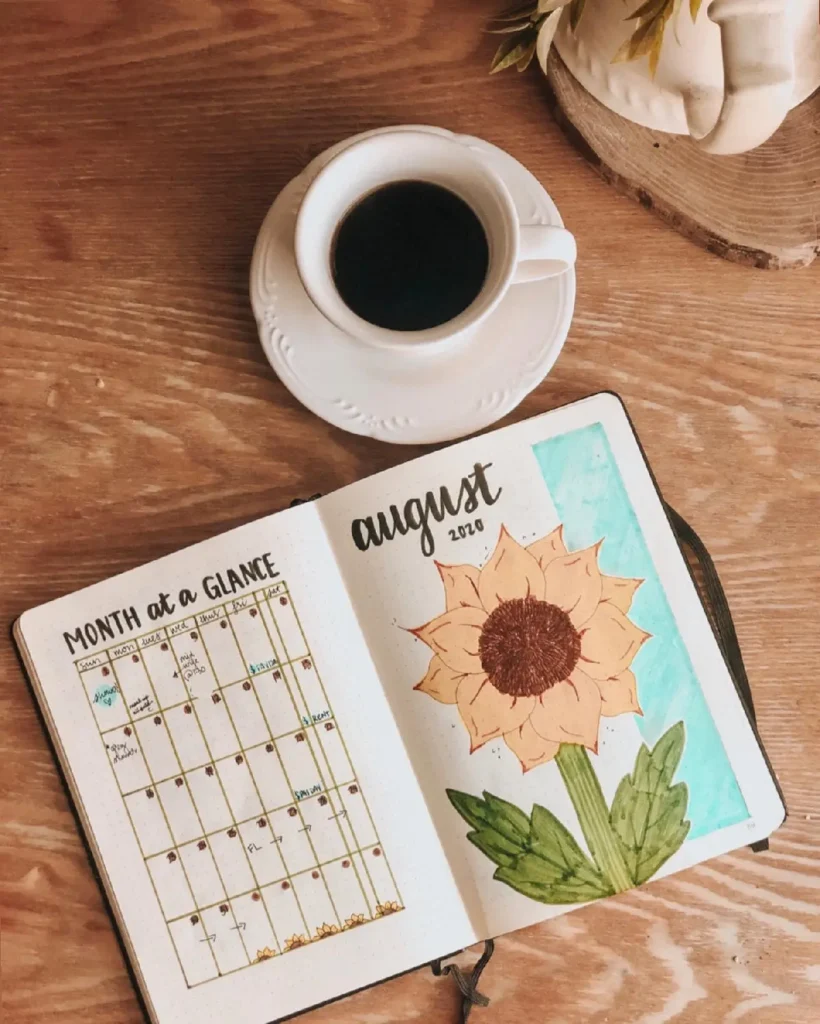 Coffee cup beside a bullet journal open to August 2020 with a sunflower illustration and monthly calendar layout.