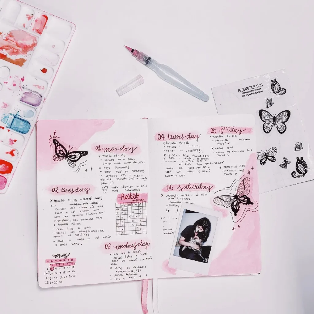 Bullet journal spread with lovely pink designs, butterflies, notes for the week, and art supplies on a white table.