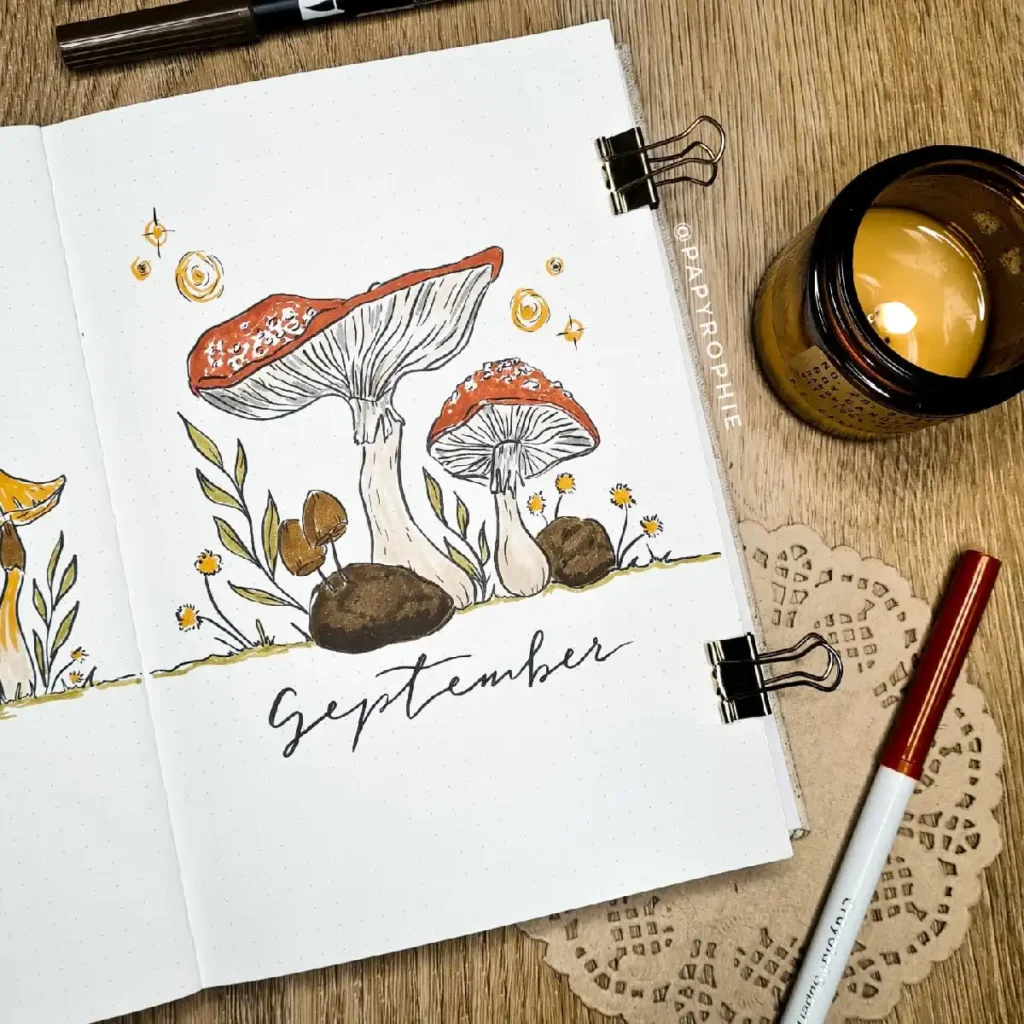 Beautiful hand-drawn mushrooms with September lettering in a cozy bullet journal setup, complemented by a candle.