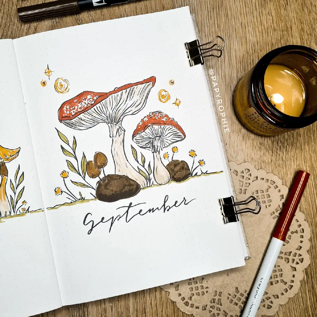 Beautiful hand-drawn mushrooms with September lettering in a cozy bullet journal setup, complemented by a candle.